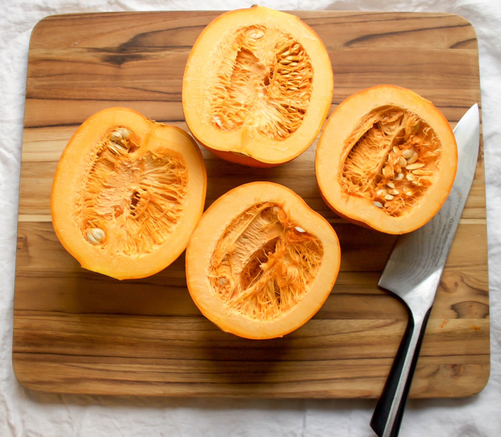 small baking pumpkins on cutting board with knife cut open with seeds in tact