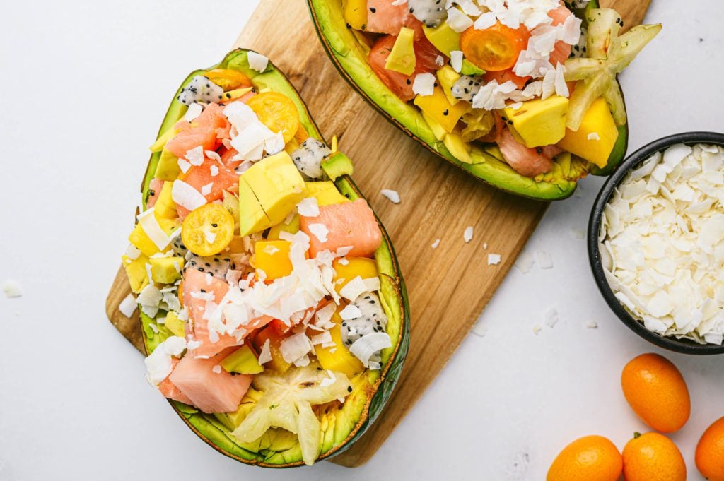 tropical fruit salad close up in avocado skin with shredded coconut