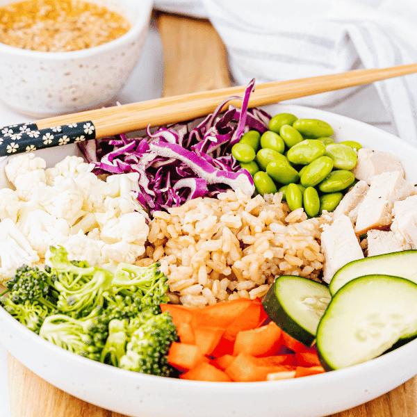 Asian Grain bowl with veggies in a white bowl with chopsticks and sauce in background