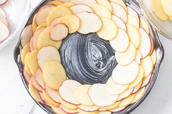 cast iron skillet layering sliced potatoes