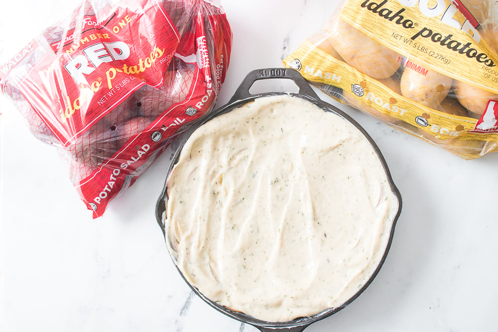 creamy cheese sauce on top of potatoes in a cast iron skillet