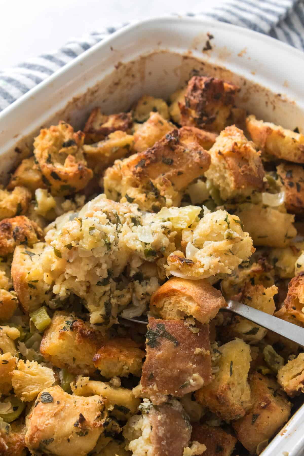 vertical close up shot of homemade stuffing recipe on spoon in casserole dish