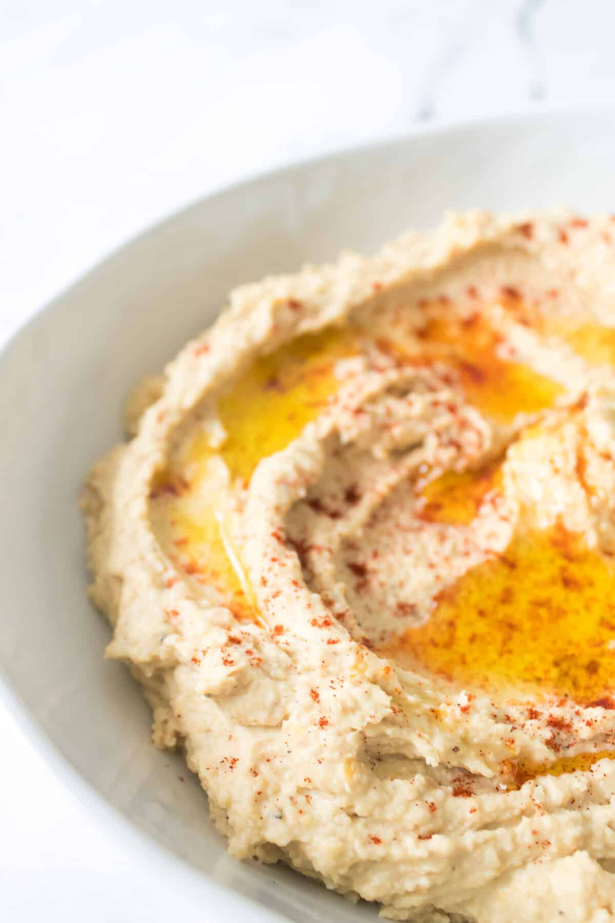 close up shot of hummus in bowl with olive oil and paprika sprinkled over top