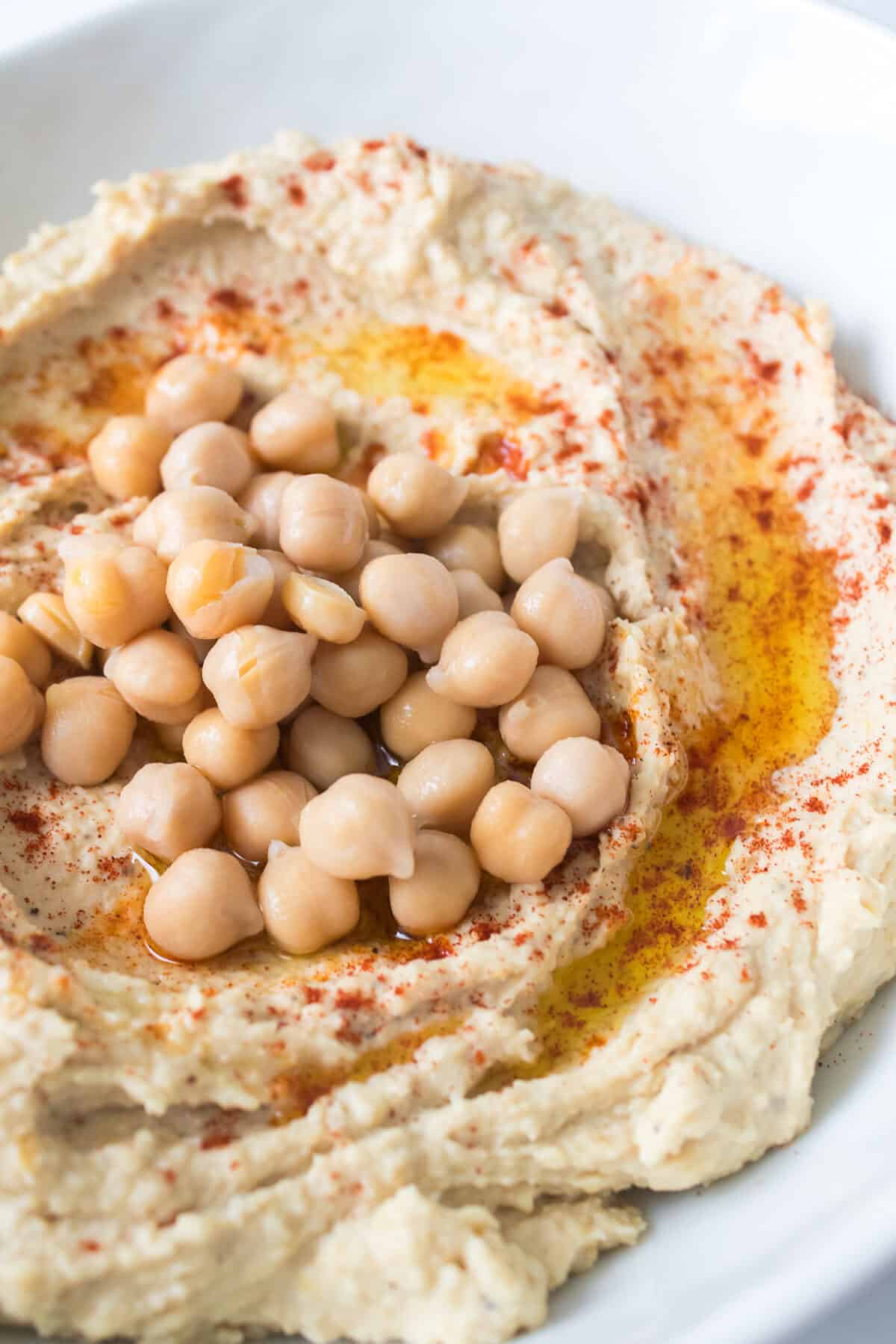 close up vertical image of chick peas on top of hummus with olive oil and paprika