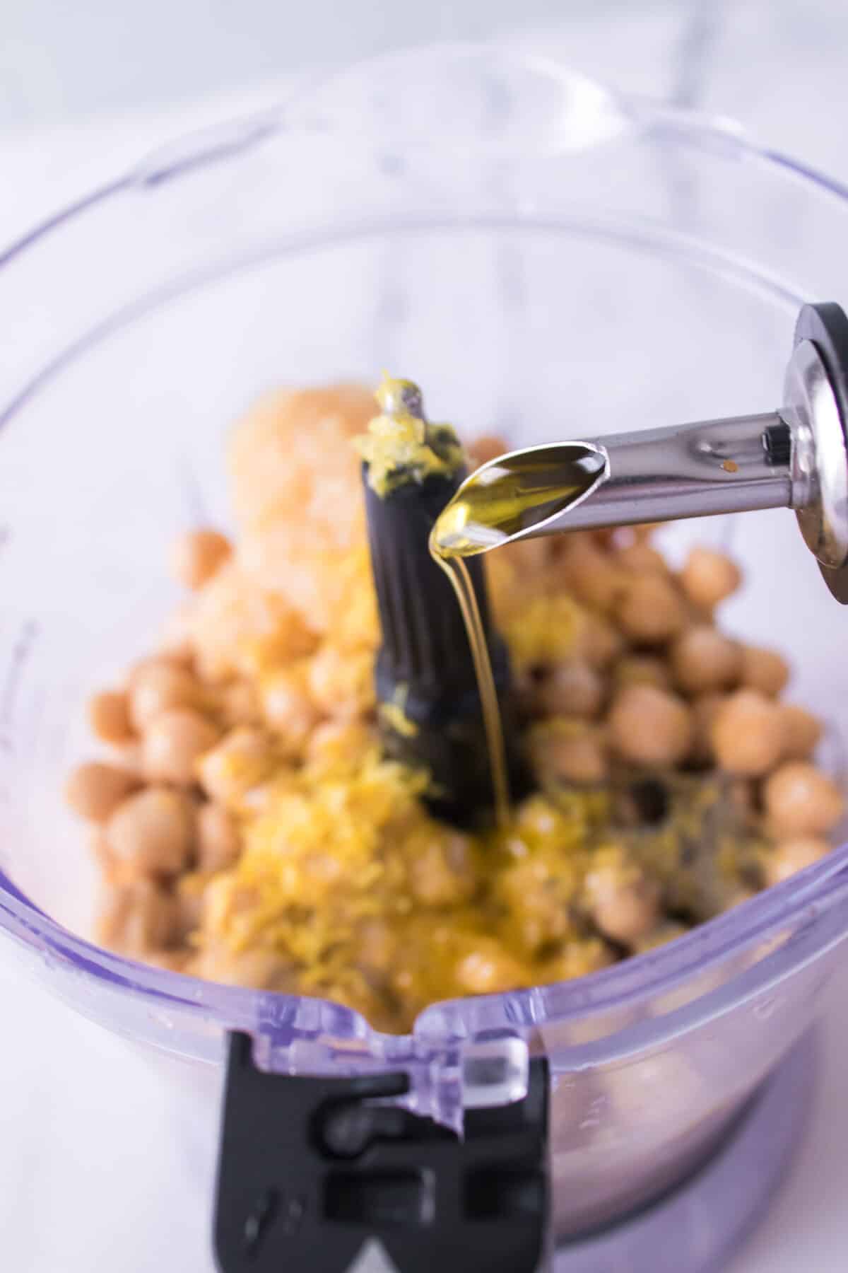 drizzling olive oil into food processor with chickpeas