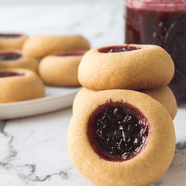 Stack of Thumbprint cookies with plate of cookies and blackberry jam in background