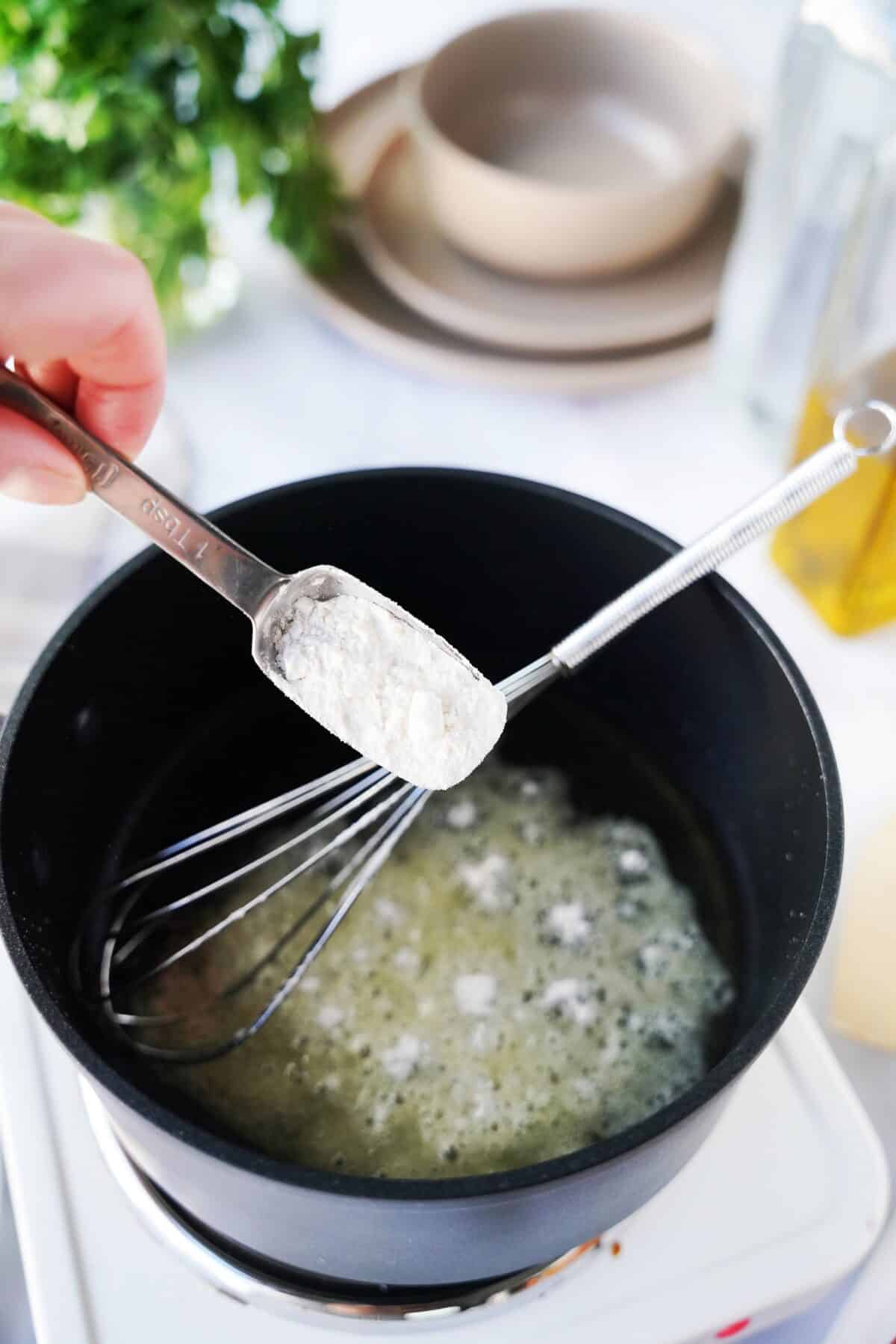 hand holding measuring spoon over sauce pain with olive and flour