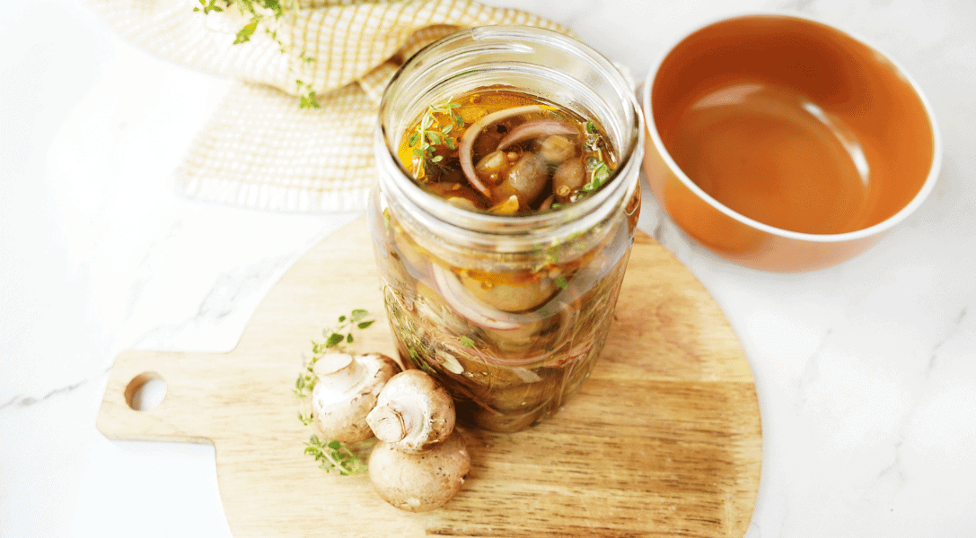 Pickled Mushrooms in bell jar on top of wood board