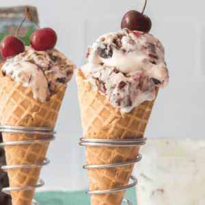 2 ice cream cones with cherry Garcia ice cream and cherries in background