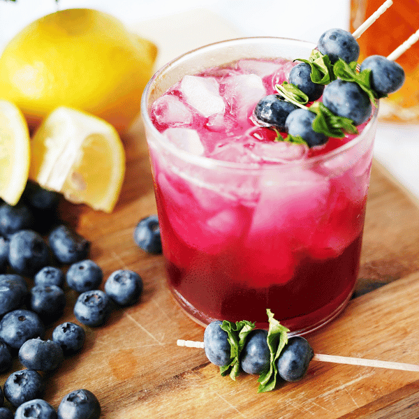 Blueberry Bourbon Smash in glass surrounded by blueberries