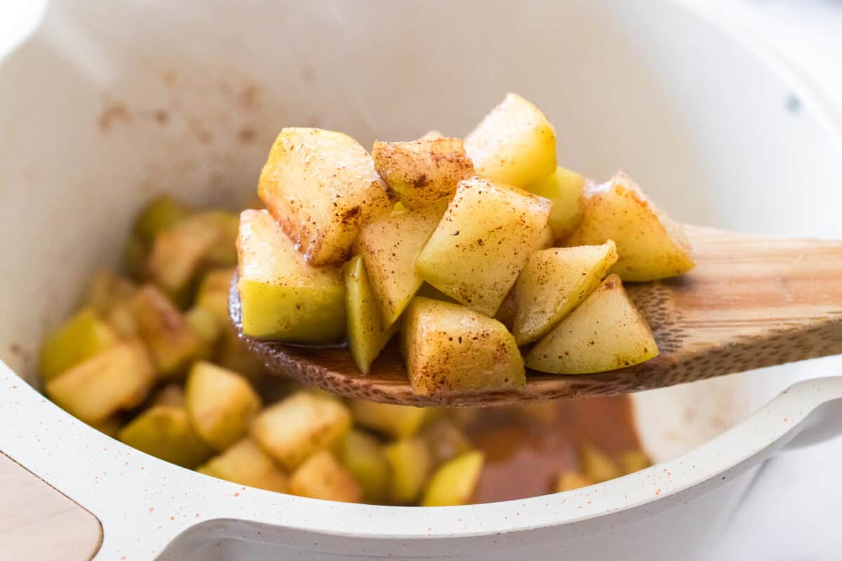 wooden spoon holding granny smith cinnamon apples over sauce pan