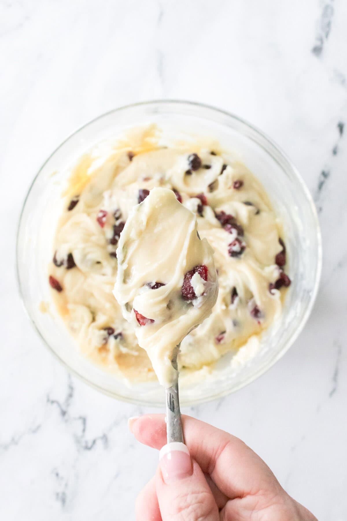 overhead shot of spoon with white chocolate, sweetened condensed milk mixed together with vanilla and dried cranberries