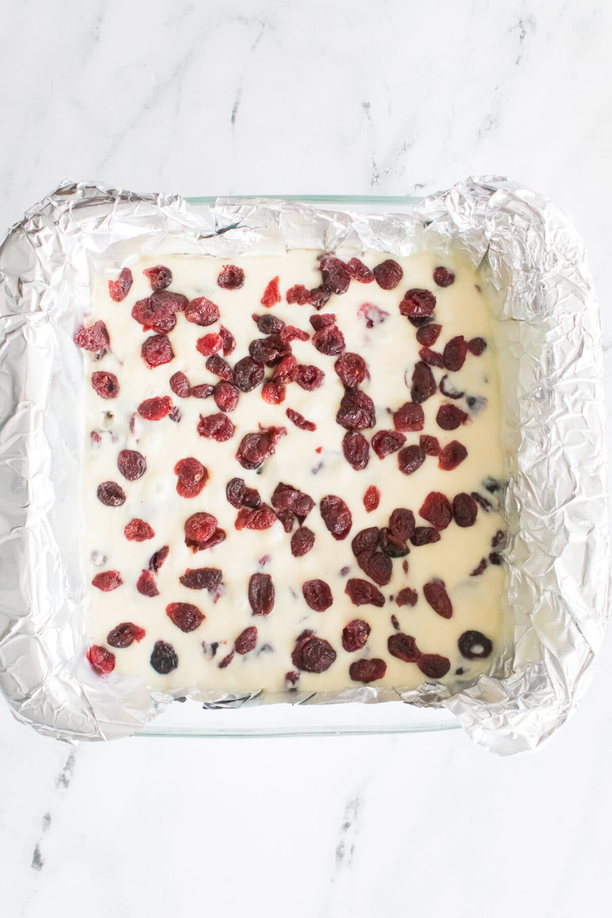 white chocolate cranberry fudge in baking dish lined with aluminum foil