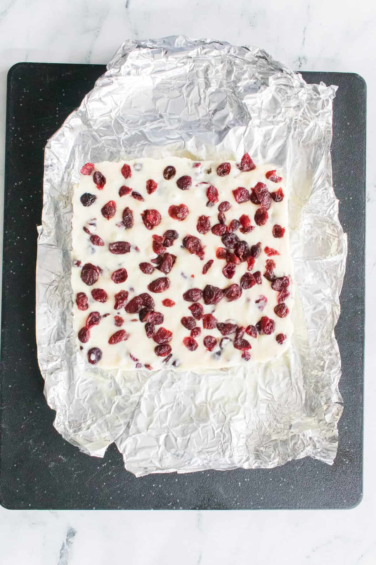 overhead shot of cranberry fudge after it has hardened on aluminum foil placed on top of cutting board