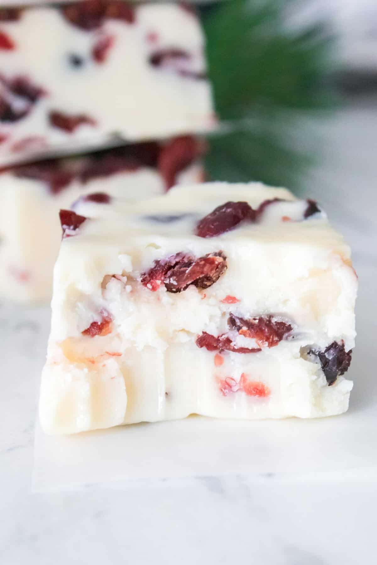 close up vertical shot of bite taken out of cranberry fudge with stack of cranberry fudge in background