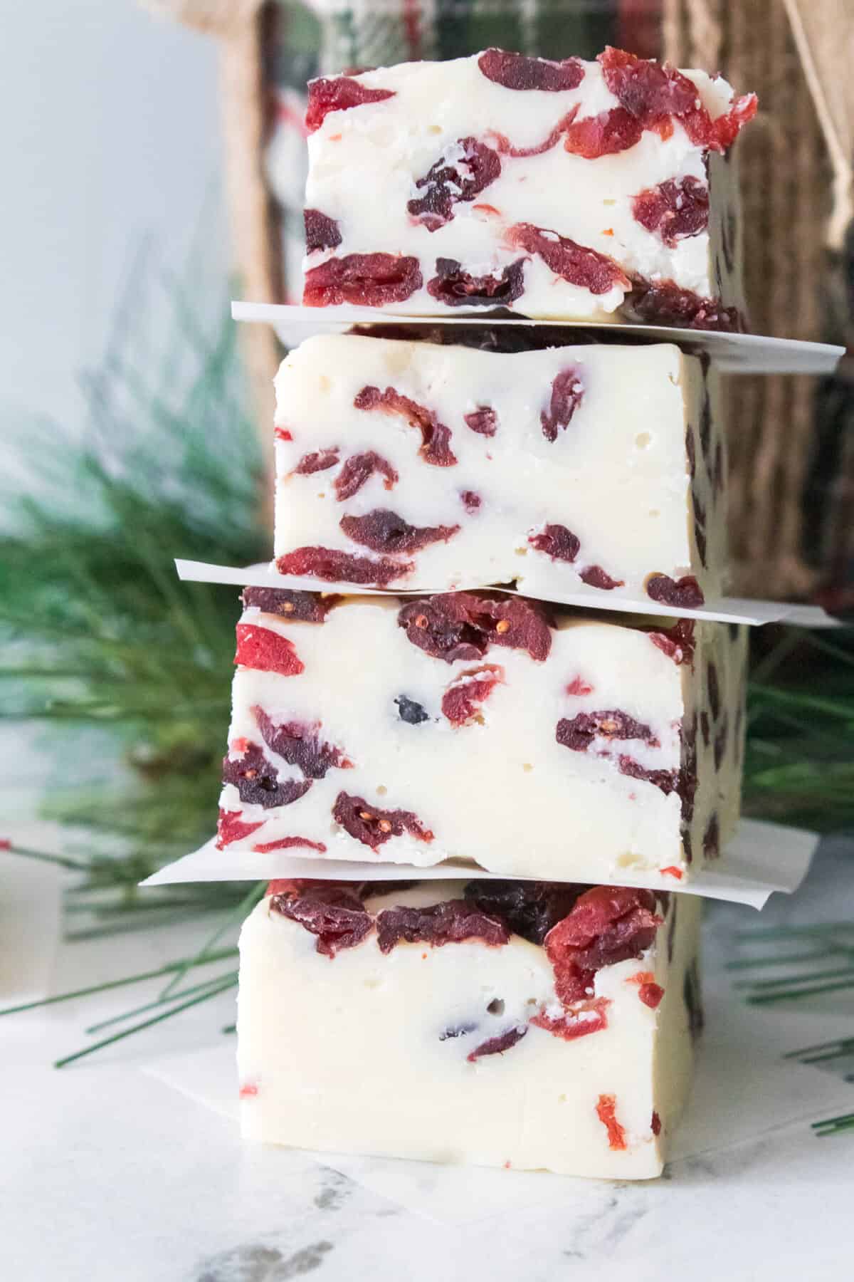 close up vertical shot of cranberry fudge stacked on top of each other with pieces of parchment paper in between