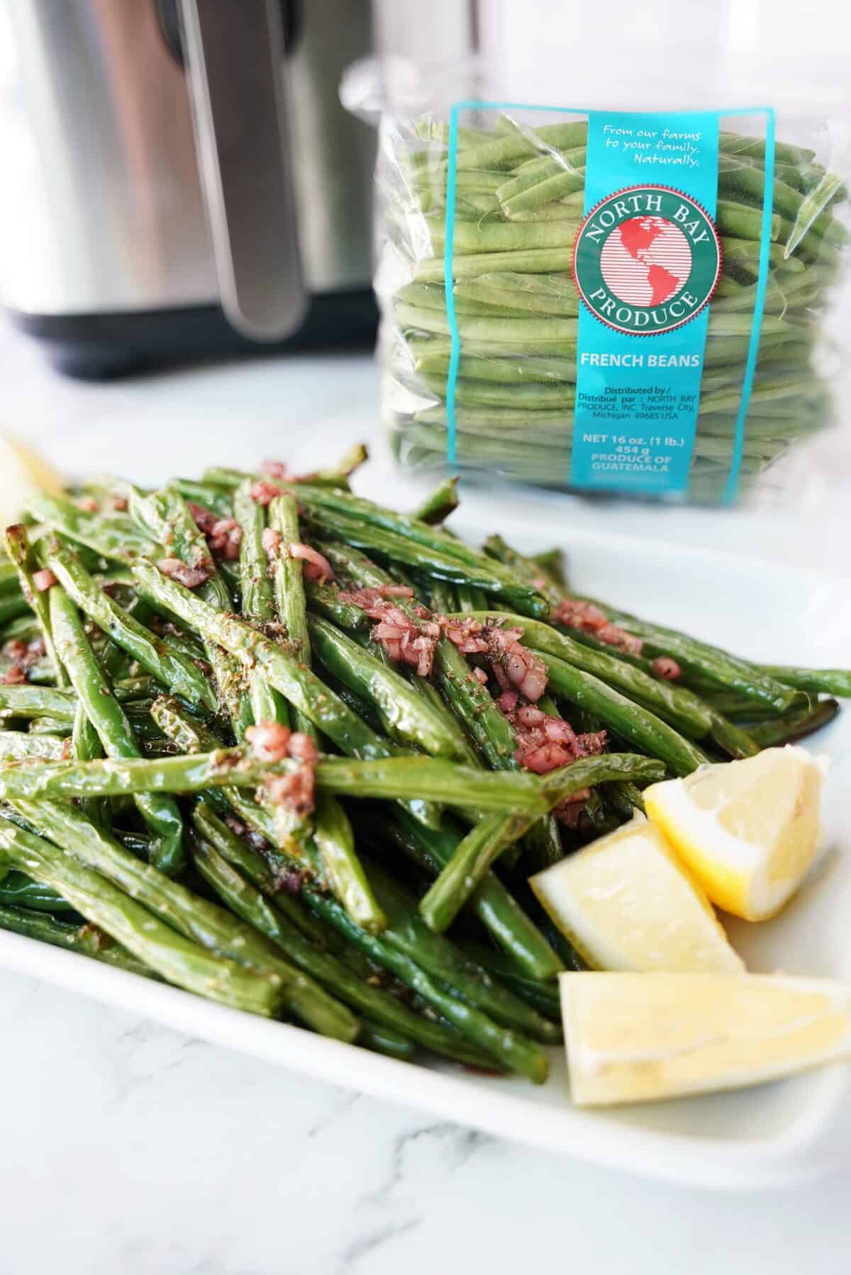 close up vertical shot of air fryer green beans plated with fresh lemons with bag of north bay produce french beans in background