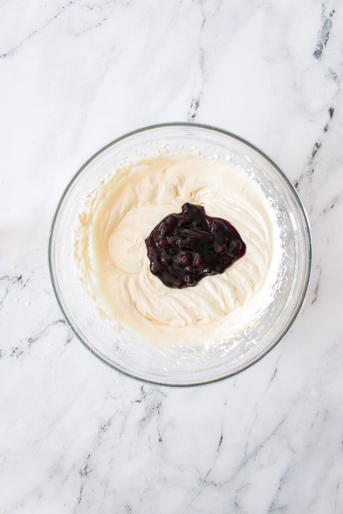 cheesecake mixture with 2 tablespoons of blueberry pie filling in glass bowl