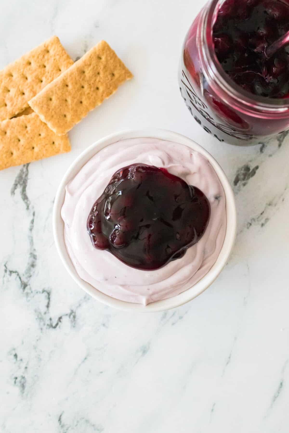 blueberry cheesecake dip in serving bowl topped with tablespoon of fresh blueberry pie fililng