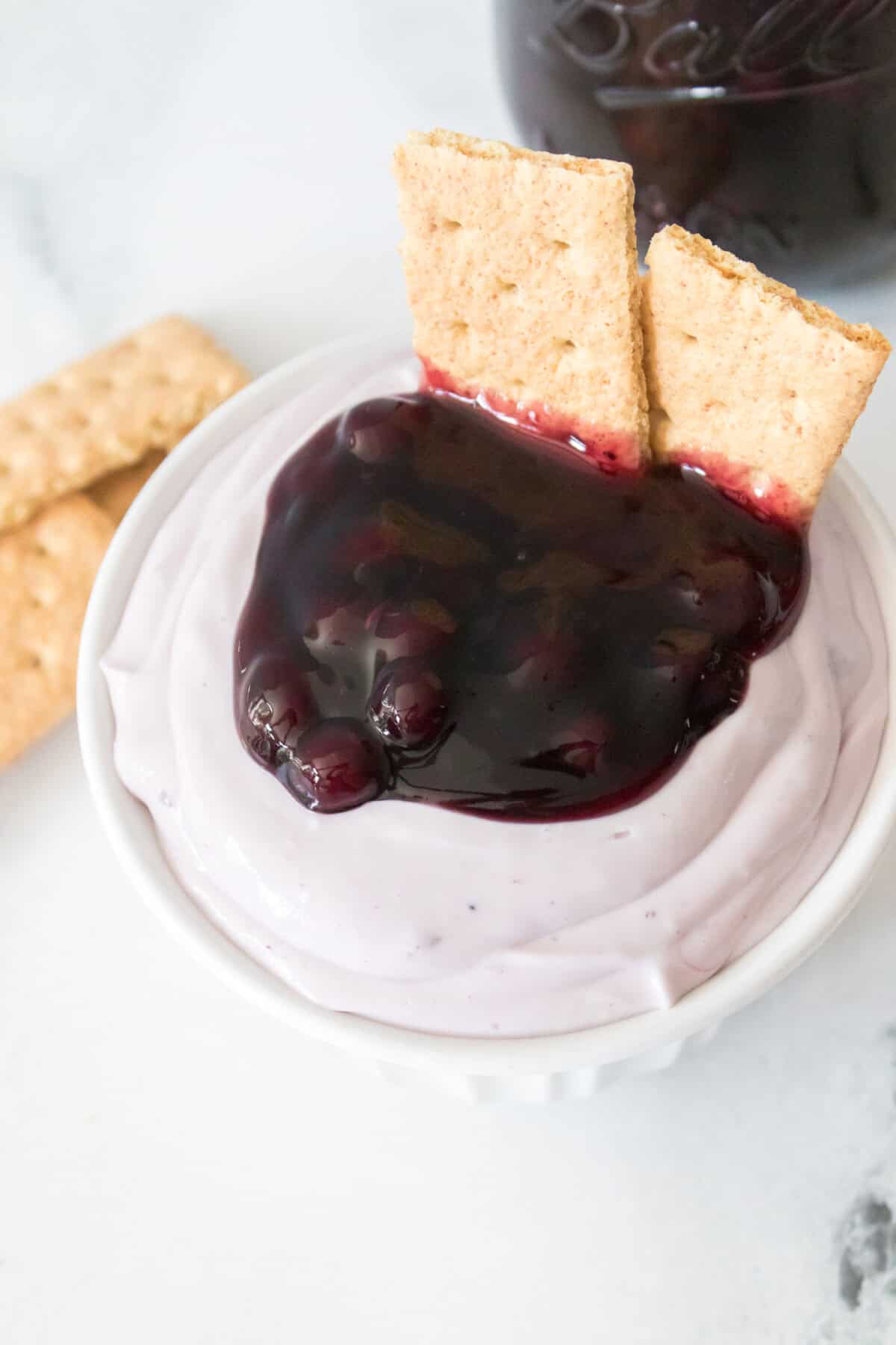 close up vertical shot of blueberry cheesecake dip with graham crackers standing up in dip