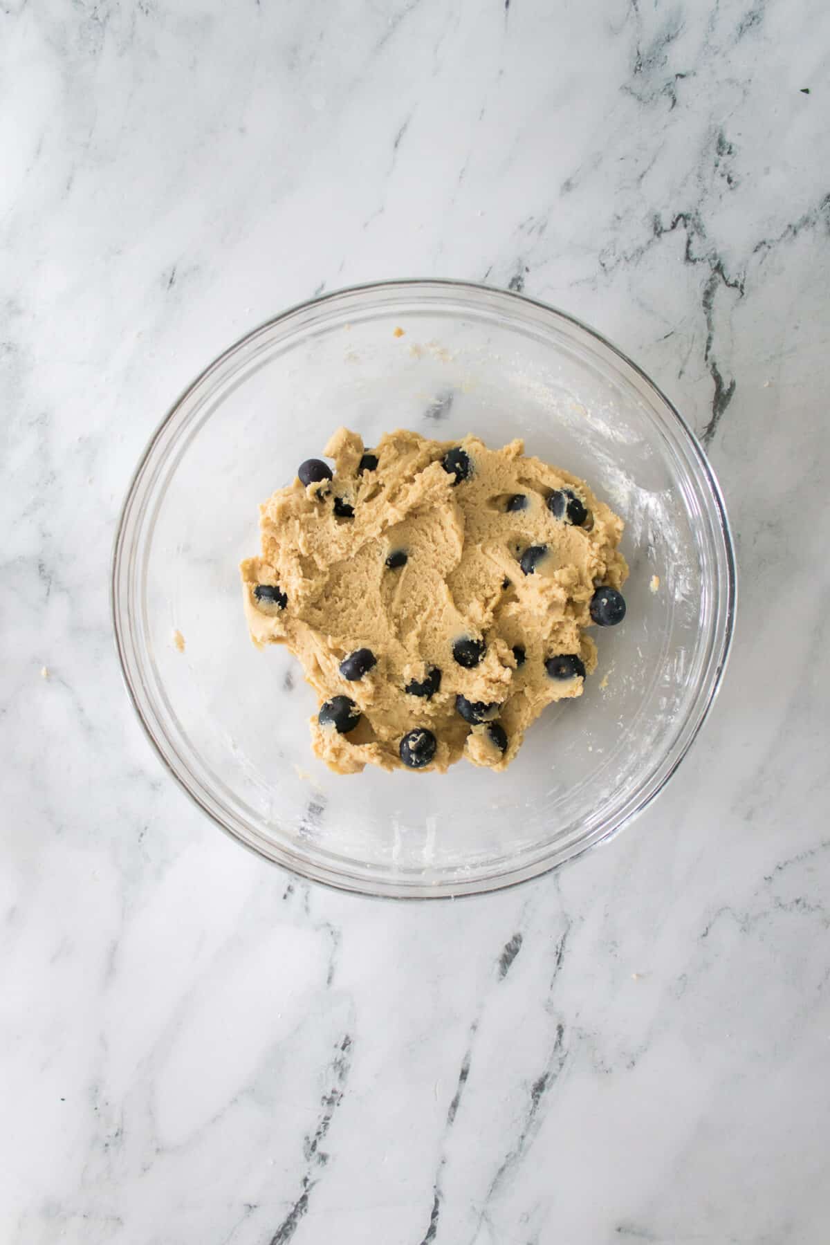 cookie dough mixed together with blueberries folded into the cookie dough in a glass bowl