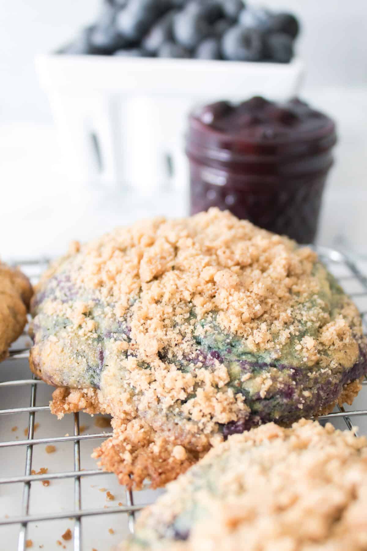 close up vertical shot of Homemade Copycat Crumbl Blueberry Muffin Cookies with blueberry jam jelly jar in background