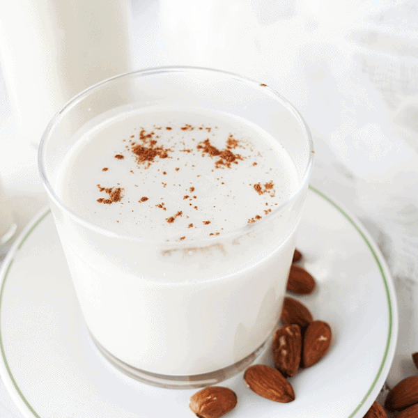 Glass of homemade almond milk with almonds on plate