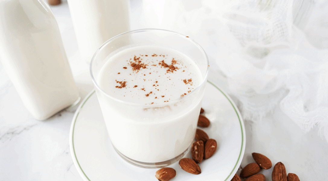 Glass of homemade almond milk with almonds on plate