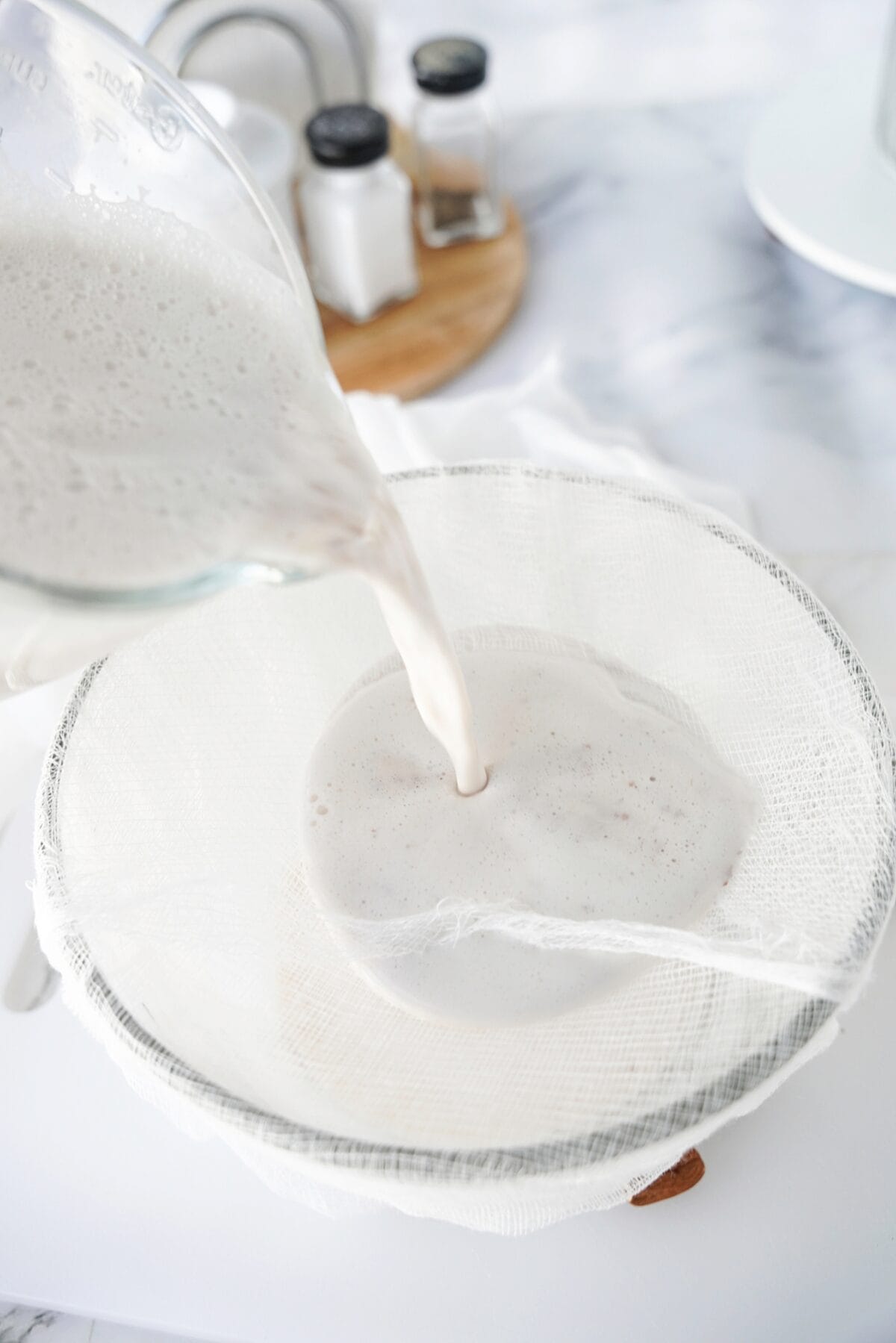 almond milk being strained with cheese cloth over glass bowl