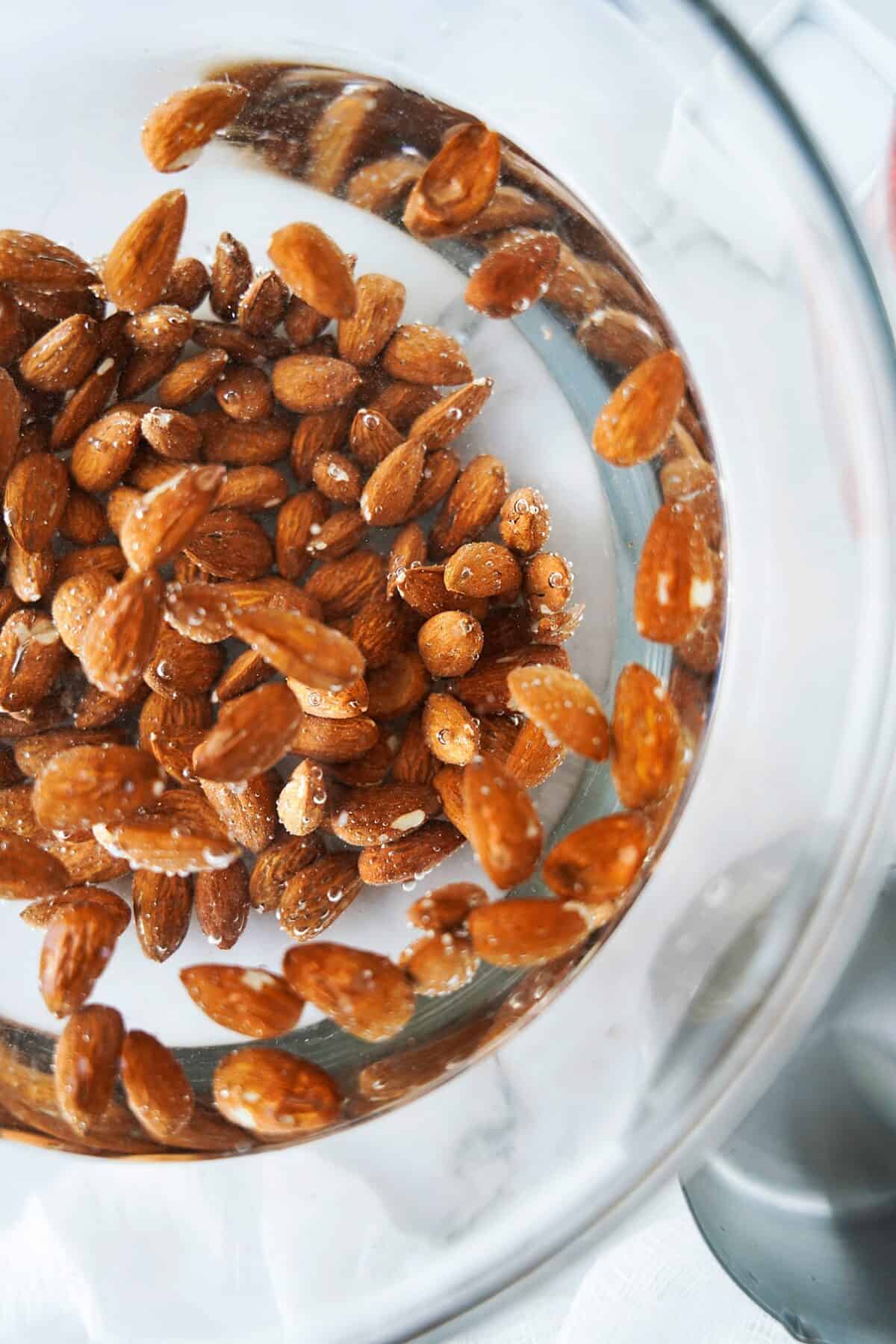 close up overhead shot of almonds soaking in glass bowl